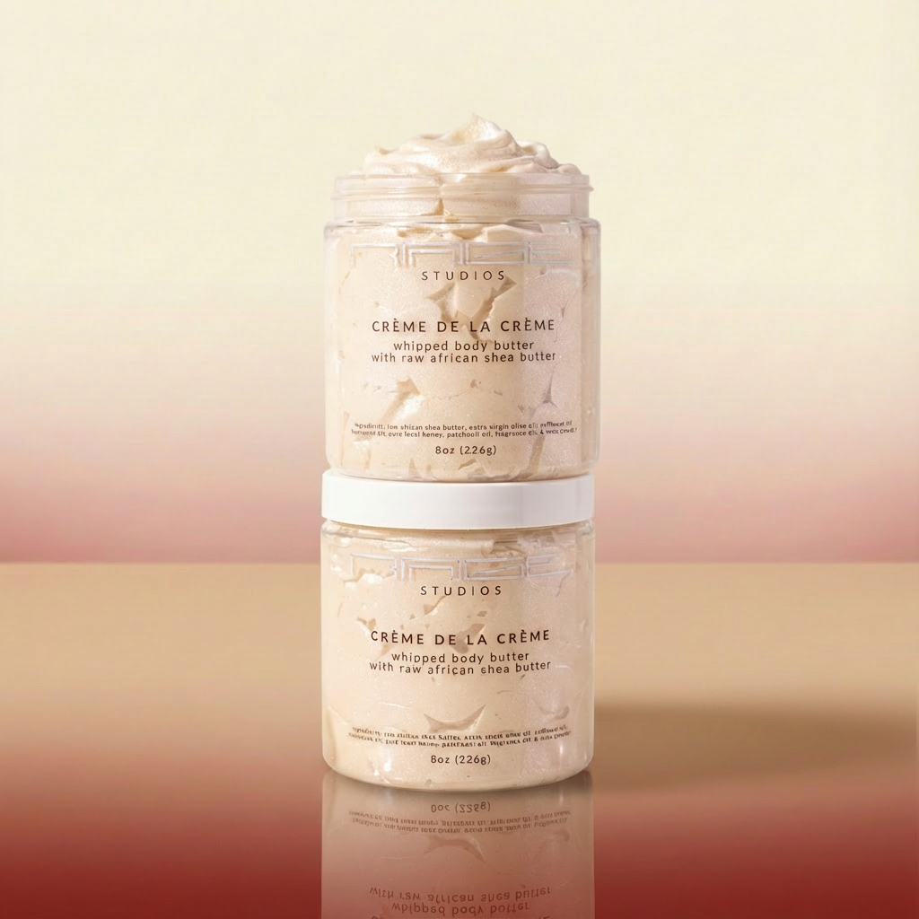 Two jars of 'Creme de la Creme' whipped body butter stacked on a reflective surface with a gradient background.